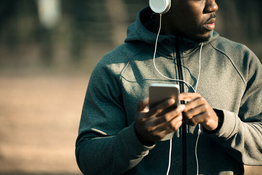 Athletic man using smartphone and headphones in park