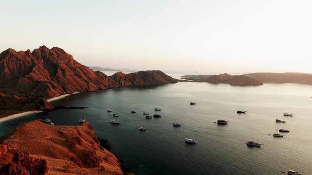 Majestic aerial view of Padar Island in Komodo National Park during a golden sunrise, showcasing the unique rugged landscape and tour boats anchored in the tranquil turquoise bay