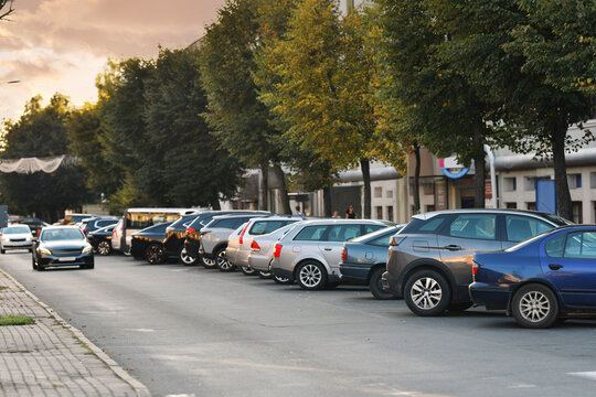 Rows of cars parked tightly along roadside in narrow residential street, urban parking shortage and crowded neighborhood transportation problem. Long row of cars parked diagonally along paved street