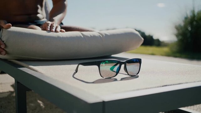 Reaching shirtless man picking up aligning placing mirrored shades on patio table to rest