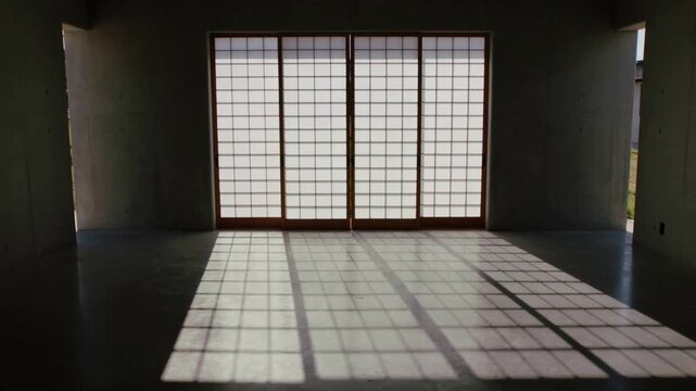 Moving sunlight through 4-panel shoji door casting growing grid across concrete floor in empty room