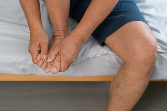 Asian old man feeling numbness and foot pain sitting in bedroom, podiatry and medical health problem
