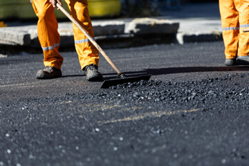 Road construction worker leveling asphalt during paving