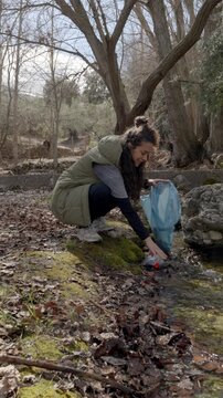 Woman activist teaching her young child about environmental care by picking up a plastic bottle from a stream in a beautiful forest