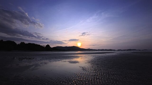 Sunset reflection across calm tidal pools on wide tropical mudflats