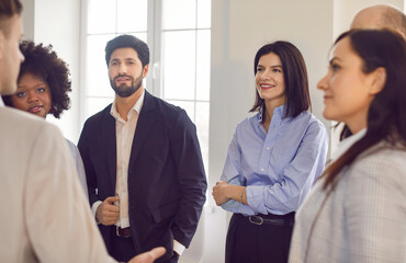 Fototapeta premium Portrait of a group of young confident diverse business people standing in office discussing job project or startups. Coworkers and company employees talking with colleague on a meeting.