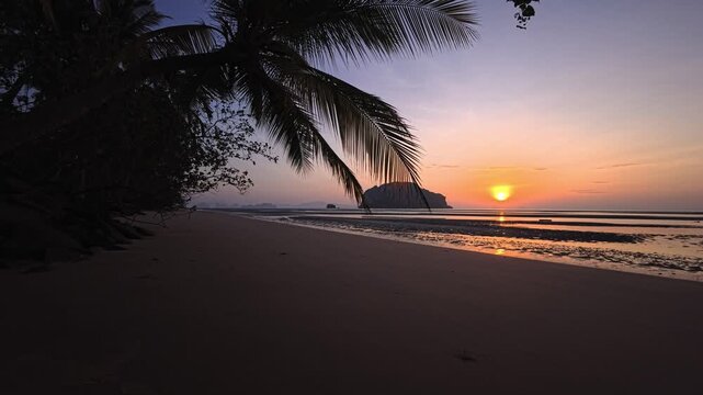 Tropical beach at sunrise with palm canopy and distant island horizon in Thailand