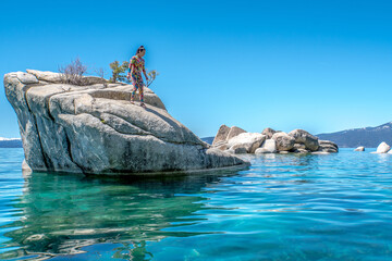 A woman is standing on a rock in front of a body of water