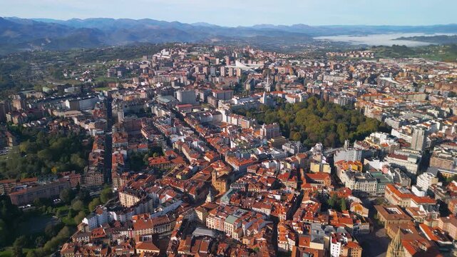 Cinematic 4K aerial orbit panorama of Oviedo city. Historic old town with orange roofs and morning fog in the mountains, Asturias, Spain.
