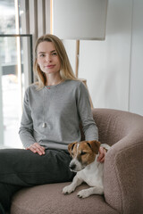 Blonde woman and dog Jack Russell terrier sitting in pink chair looking at camera. Natural light....