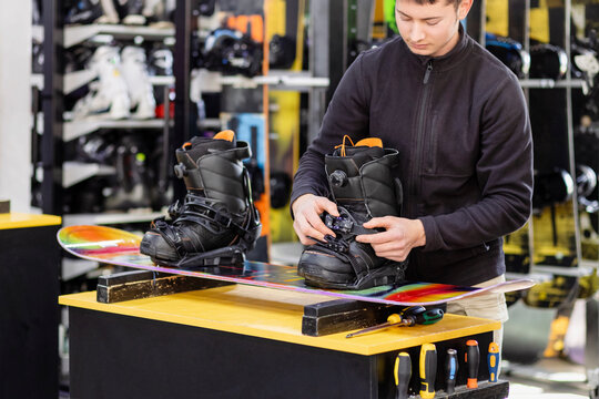 Snowboard Boots for Rent. Worker Adjust Bindings in Ski Rentals Center. Technician Adjusting Snowboard Boots Before Riding. Snowboard Equipment Fitting at Ski Center. 