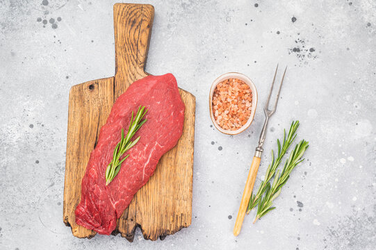 Raw beef inside round topside with herbs and seasoning on cutting board. Fresh lean red meat prepared for cooking on light rustic background.