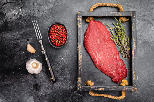 Fresh raw beef inside round topside with thyme herb and garlic on wooden tray. Lean butcher cut meat on dark background, top view.
