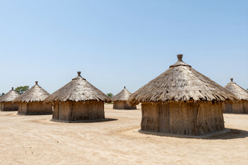 Traditional Thatched Huts Arranged in a Row on Sandy Ground under Clear Blue Sky Rural African Village Settlement Lifestyle Photography