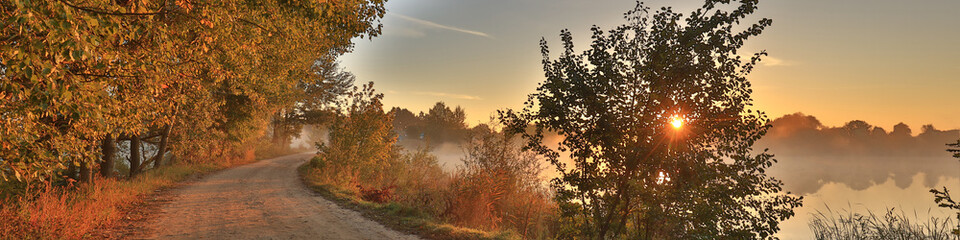 Fototapeta premium Early foggy morning, sunrise over the lake. Rural landscape. Dirt road along the lake. HDR