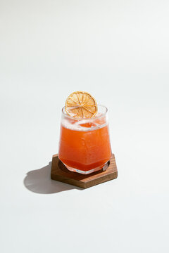 Refreshing Orange Drink with Dehydrated Citrus Garnish on Wooden Coaster.