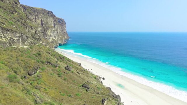 Aerial view of high rocky cliffs bordering a white sand beach and turquoise ocean water on Socotra Island, Yemen.