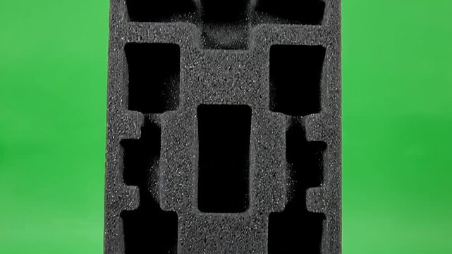 Detailed view of custom-cut black foam cushioning designed for product protection, showcasing secure packaging solutions on a bright green screen