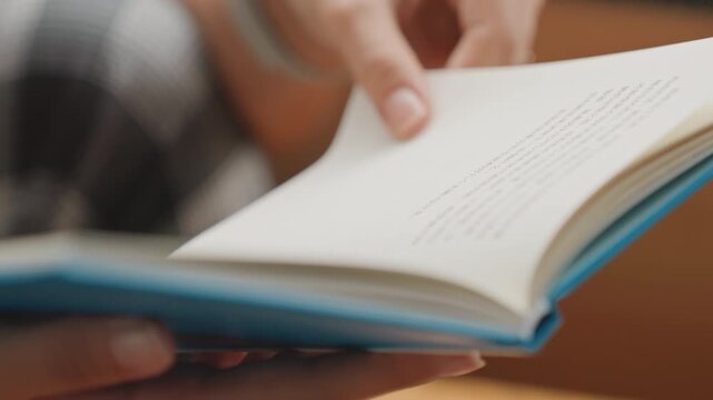 Hands flip pages. Relaxed reading in hotel lounge. Contemplative travel moment with book and casual outfit. Pair of hands flipping pages with smartwatch and plaid clothing visible in background