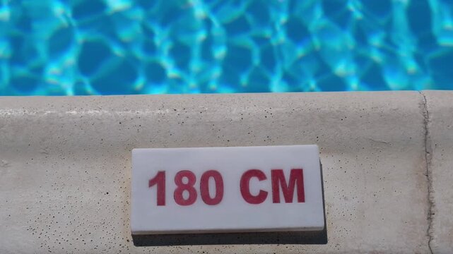 Water depth indicator reads 180 cm on the pool edge, surrounded by sparkling blue water under sunlight in a vibrant outdoor environment