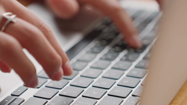 Freelancer composing article on wooden desk. Individual typing on keyboard with rings in warm sunlight. Creative writer concentrating on article at hotel workspace with sunlight and rings
