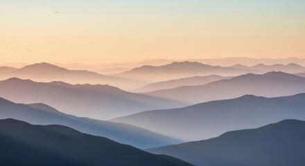 Layered mountain ranges recede into a hazy, soft orange and blue sunrise