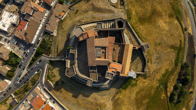 Zenithal view of the Castle of Melfi in Basilicata, Italy. It's a medieval stone castle, revealing its complex geometric layout of courtyards, fortified walls, and tiled roofs surrounded by dry slopes