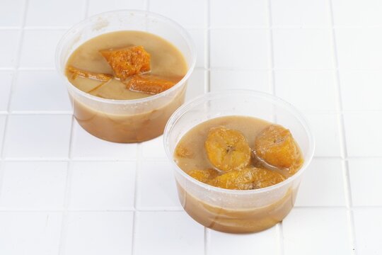 Traditional Indonesian kolak pisang and kolak labu kuning dessert made from banana and pumpkincooked in coconut milk and palm sugar served in plastic takeaway cup.