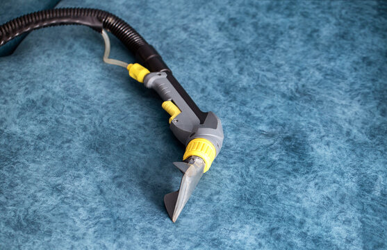 Cleaning nozzle of washing vacuum cleaner on blue upholstery. Equipment for deep cleaning of sofa fabric or carpet surface. Professional home hygiene service.