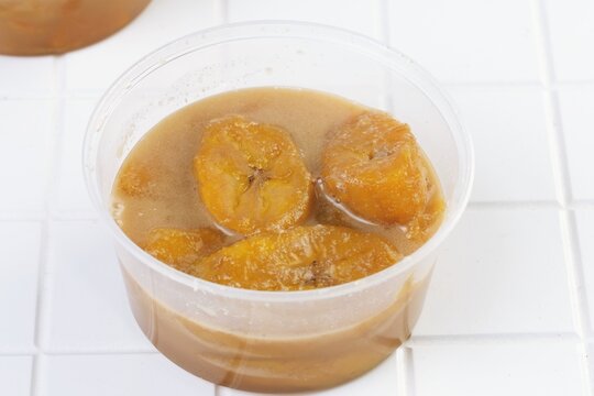 Traditional Indonesian kolak pisang dessert made with banana in sweet coconut sugar sauce served in plastic bowl.