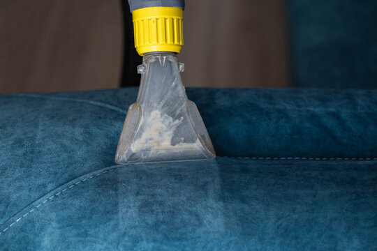 Deep cleaning of a blue upholstered sofa using a cleaning tool for dirt removal