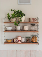 A wooden shelf with tea and coffee utensils, decor, a cookie jar and a homemade flower on the kitchen wall © okkijan2010
