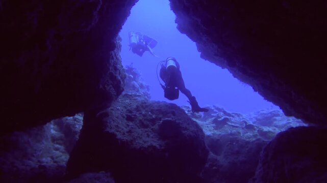 following lookout from a dark triangle cave to two divers in front diving coming out from the cave while scuba diving in the deep ocean sea salt water underwater world during day time in Lanyu Taiwan 