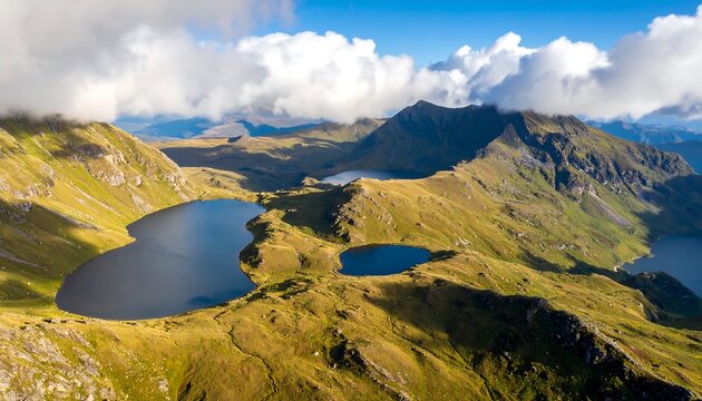 An aerial panorama showcases rugged, mountainous terrain and several placid lakes, framed by clouds in a bright blue sky