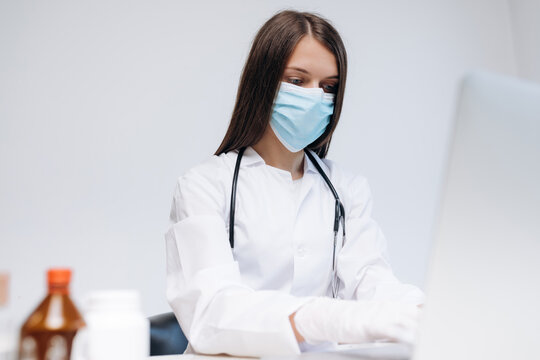 Female doctor wearing mask and gloves working on a computer in clinic for telemedicine