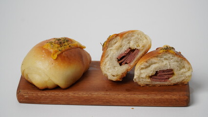 Isolated white soft sourdough salt bread topped with melted cheddar cheese and parsley, filled with smoked beef and cheese, placed on a wooden brown plate.