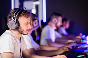 Bristly gamer in headset playing video game at computer club, cyber sport tournament. E-sport championship. Player in headphones communicates with others over mic. Multiplayer online competition © HENADZY