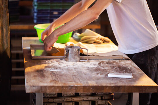 Baker hands preparing dough on wooden table, sifting flour for artisanal bread production, showing traditional manual creation of bakery goods