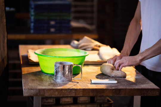 Professional baker hands kneading raw dough on wooden table for fresh bread preparation in bakery kitchen, artisanal food production