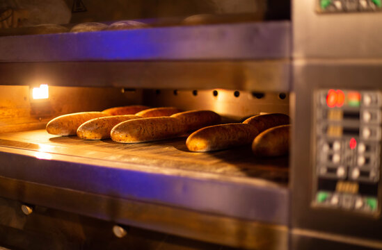 Golden brown bread baking in commercial bakery oven, light illuminating fresh baked goods inside industrial kitchen equipment, close up view of warm fresh loaves