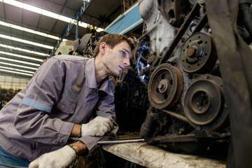 Young worker engineer man in safety protective uniform holding walkie talkie while inspecting engine in factory. Industrial labor working and repairing machinery at auto parts manufacturing industry.