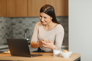 Focused young entrepreneur working remotely from home kitchen with digital devices.