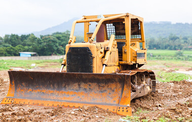 Old bulldozer parked on construction site with soil and dirt around, heavy machinery used for land clearing, road building and earthmoving work in rural landscape.