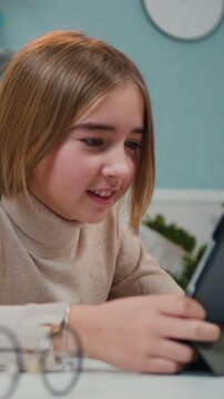Close up of cute and hapy little girl uses tablet device while sitting at the desk in the living room. Child has fun while plays Internet games, enjoy winning the computer game. Slow motion