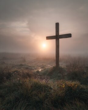A lonely wooden cross in a field covered in thick morning mist. 