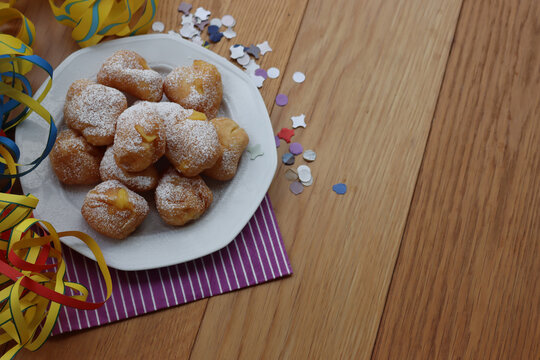 Traditional italian fritters filled with cream called Frittelle on a plate on wooden table with colorful paper streamers and confetti with copy space