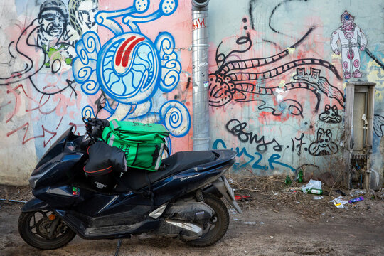 Warsaw, Masovian, Poland - February 28 2026: A black Honda PCX scooter with a green delivery bag against a weathered concrete wall covered in vibrant, chaotic street art.