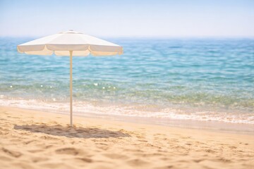 A Tranquil Beach Scene with a White Umbrella Casting Shade on the Golden Sand Beneath a Clear Blue Sky Overlooking Calm Ocean Waves