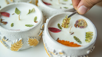 The master's male hand decorates scented candles with colored leaves with tweezers. Decorating Scented Gypsum Container Candles In Workshop © Rystemys
