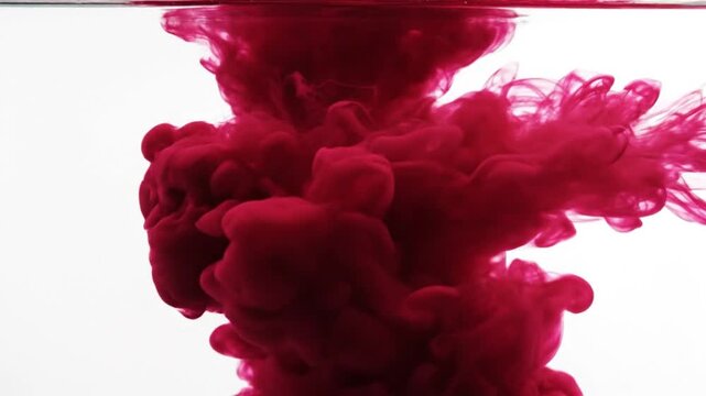Red ink dissolving in clear water, creating abstract cloud-like shapes and patterns.